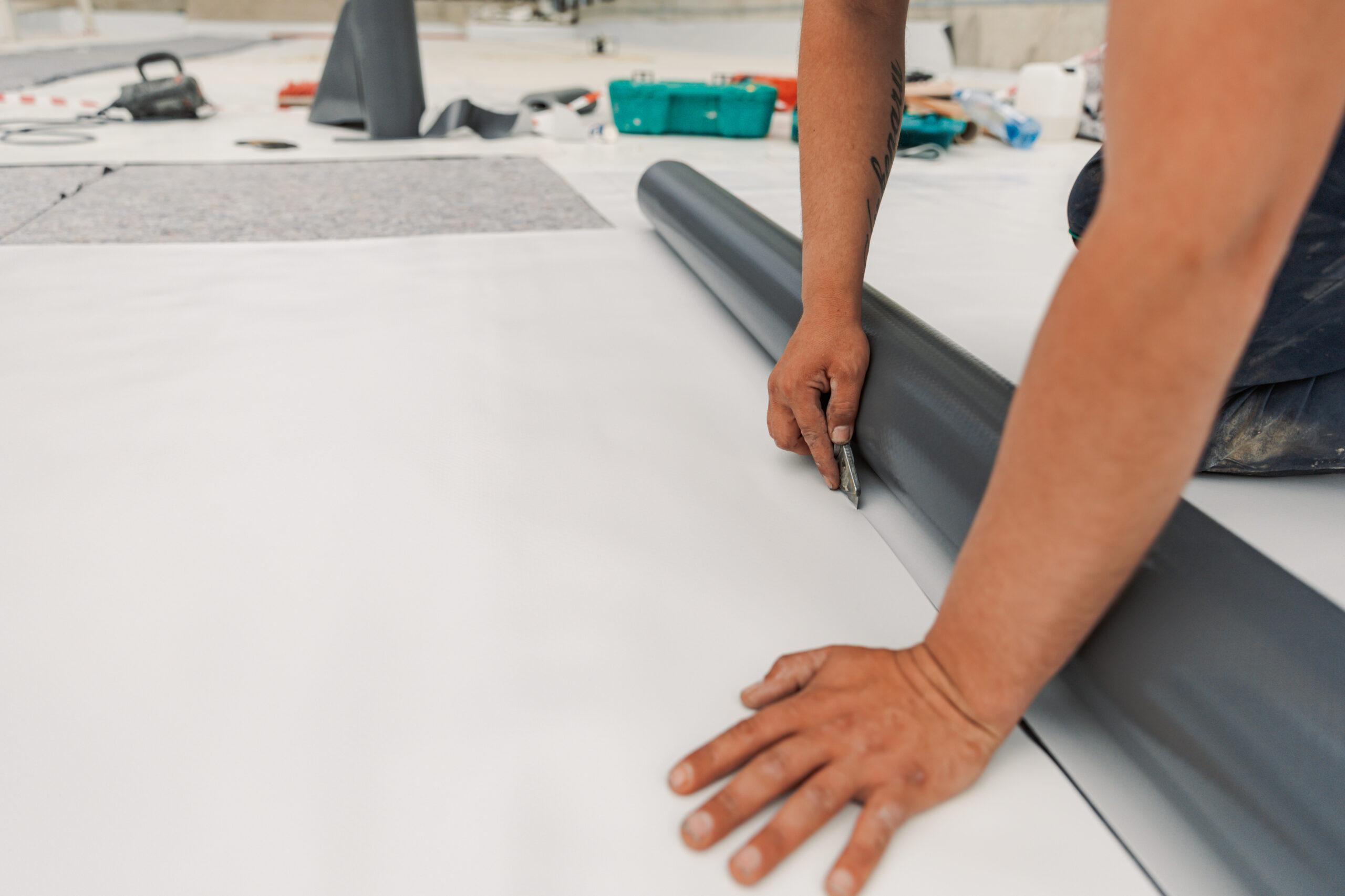 Worker Cutting TPO Roofing On Commercial Roof